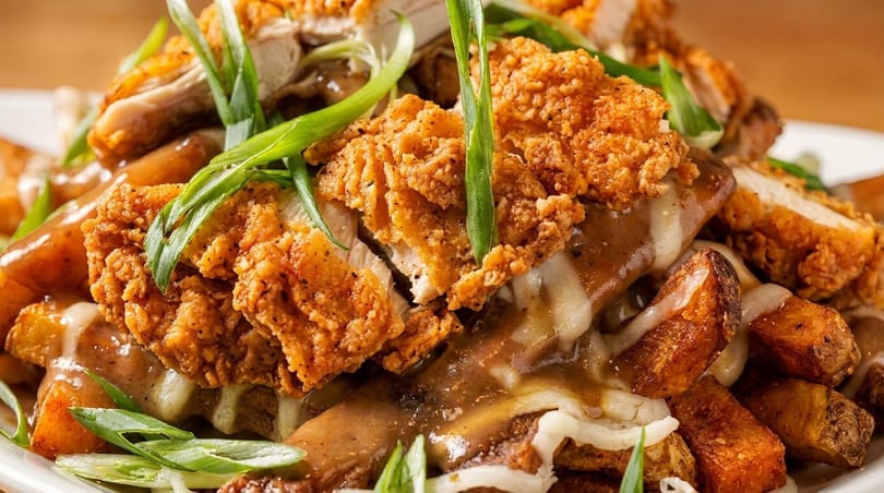 Crispy fried chicken pieces, gravy, cheese curds, and potato wedges, garnished with green onions.